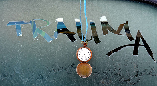 Trauma written on frosted glass with an open pocket watch dangling in foreground